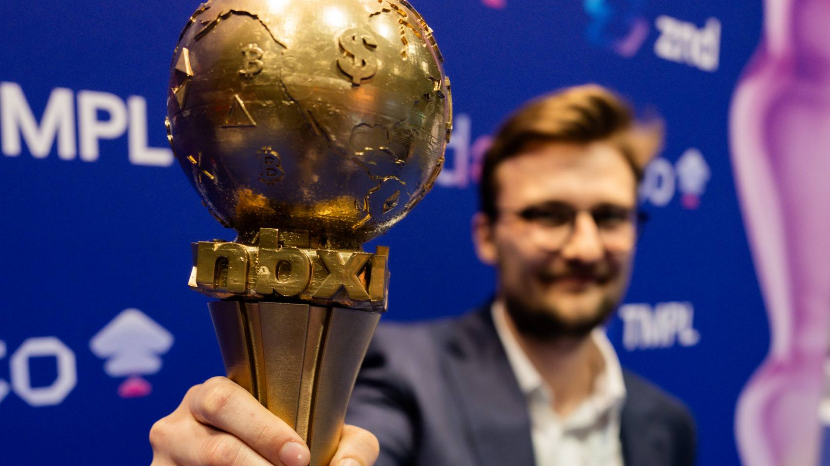 A man holding a golden NBX trophy shaped like a globe with currency symbols against a zondacrypto logo background.