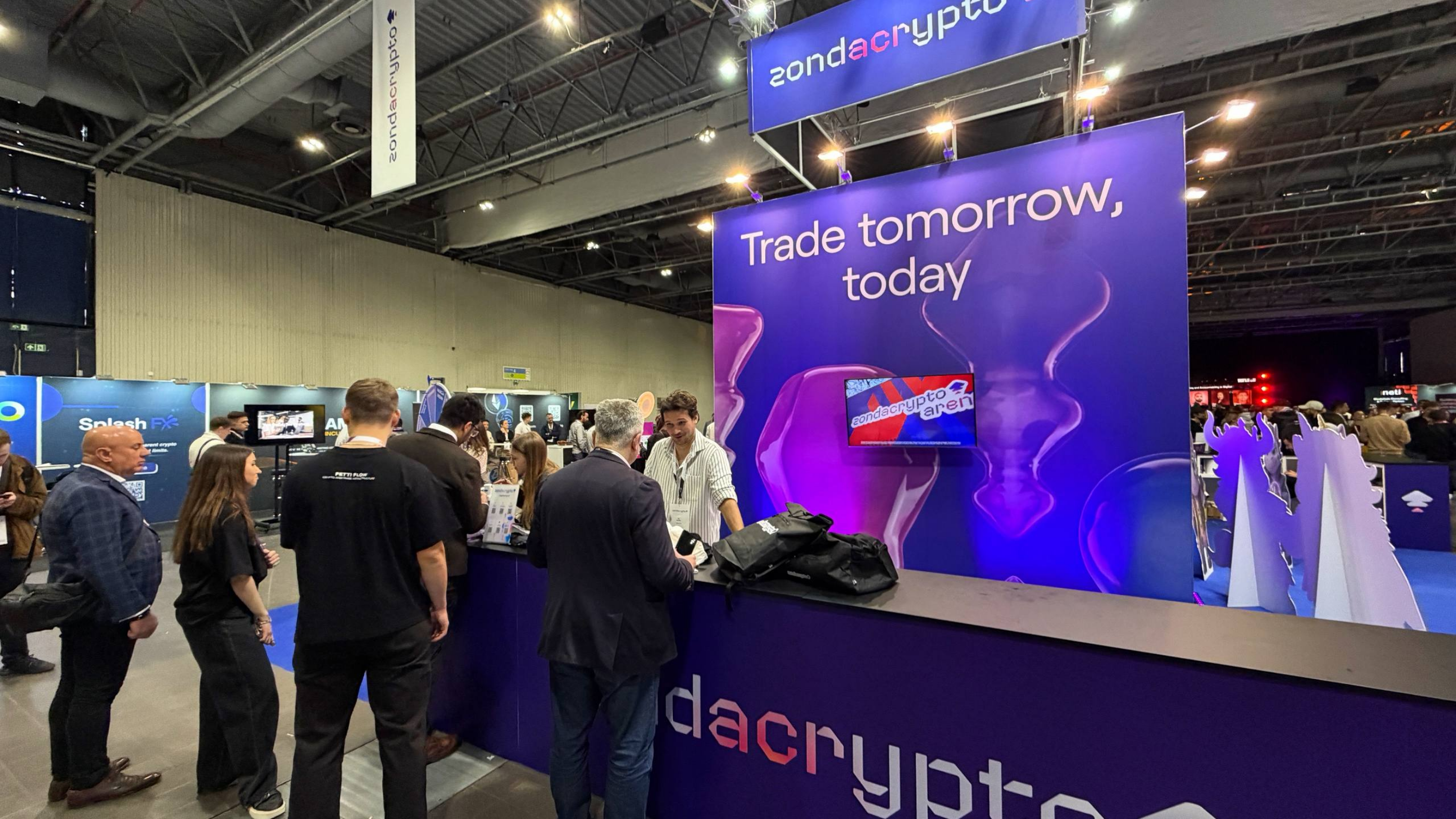 View of the zondacrypto booth at an expo with the slogan "Trade tomorrow, today" and people at the counter.