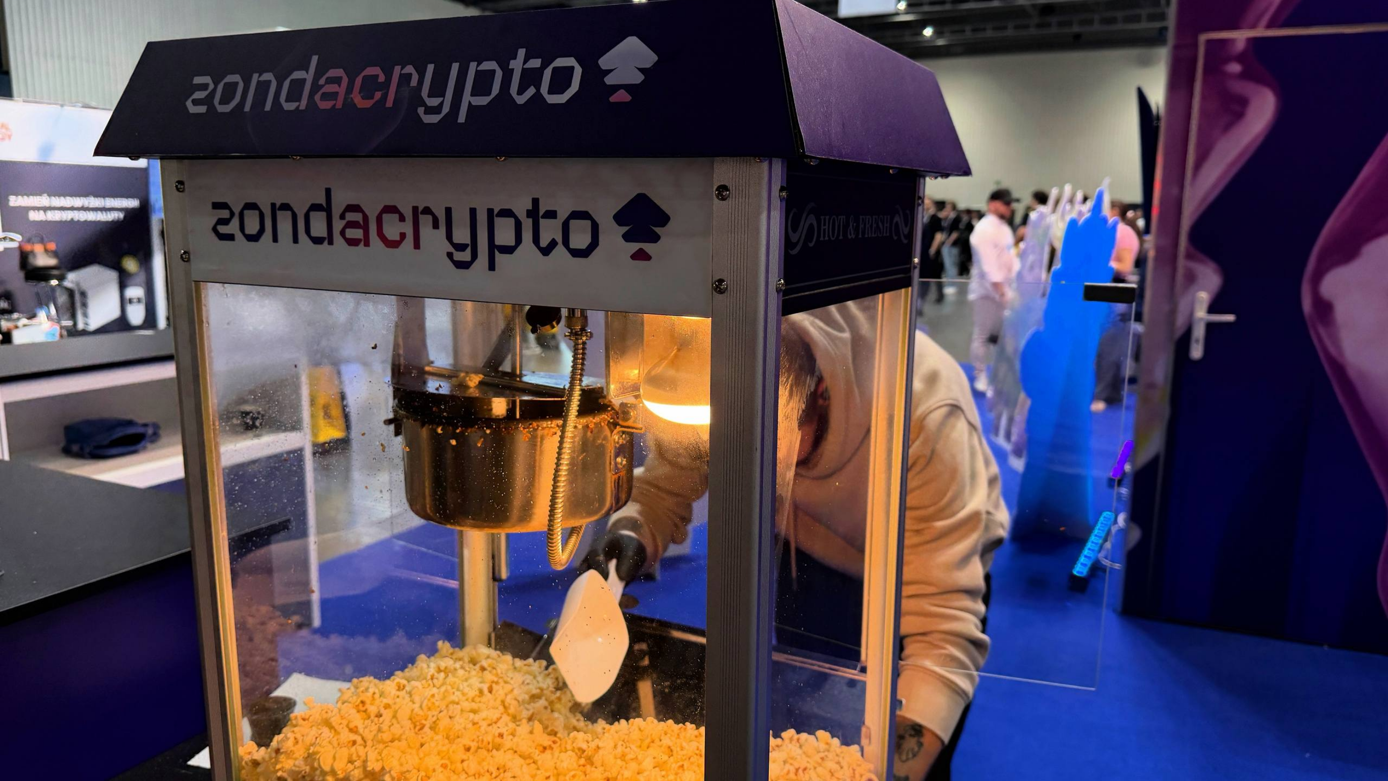 Close-up of a popcorn machine branded with zondacrypto logos during an event.